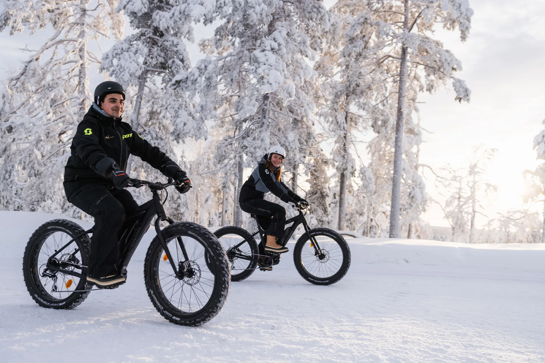 A couple fat biking across the snow near Octola III in Finnish Lapland