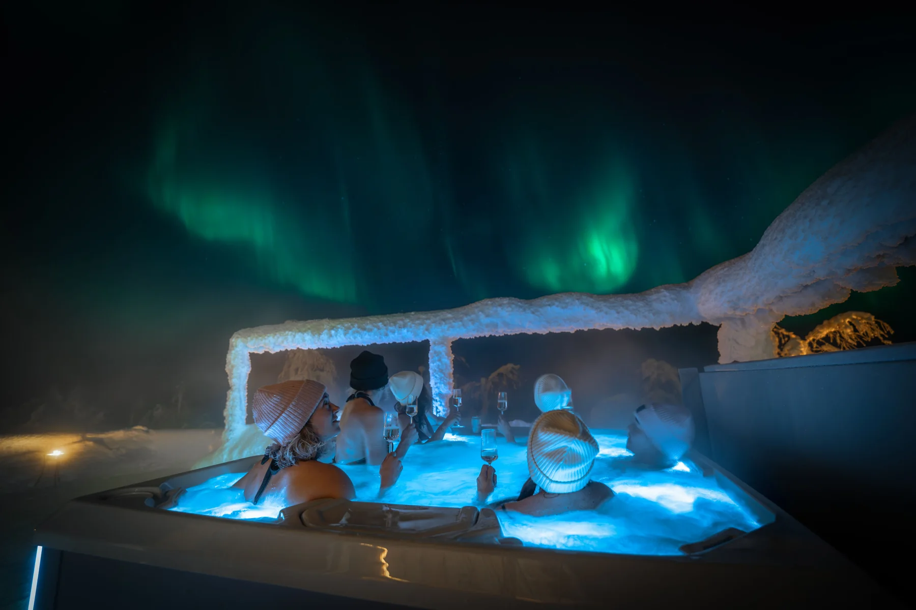 Guests in an outdoor hot tub under the aurora at Octola Private Wilderness