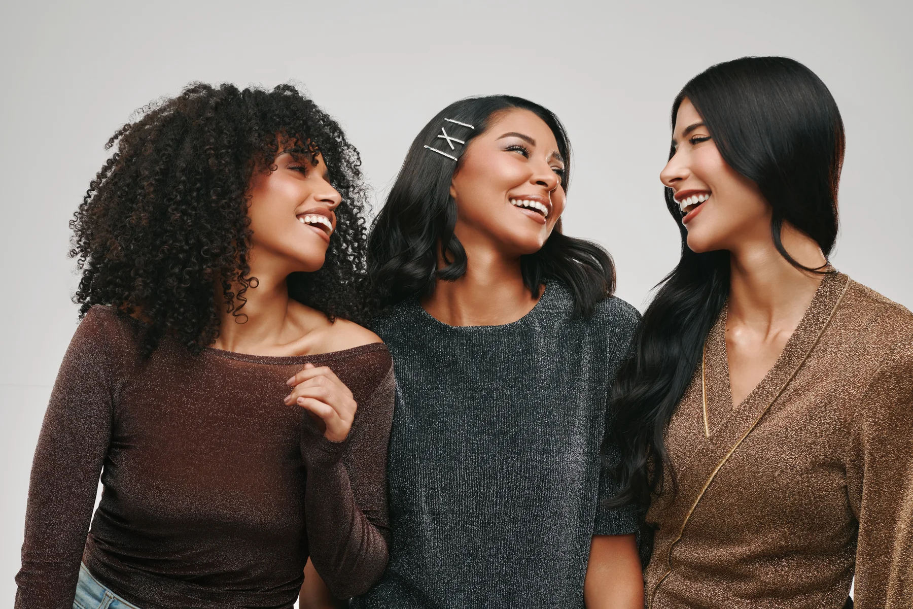 Three friends in knitwear laughing together in a Sephora beauty campaign, one wearing a Sephora hair clip