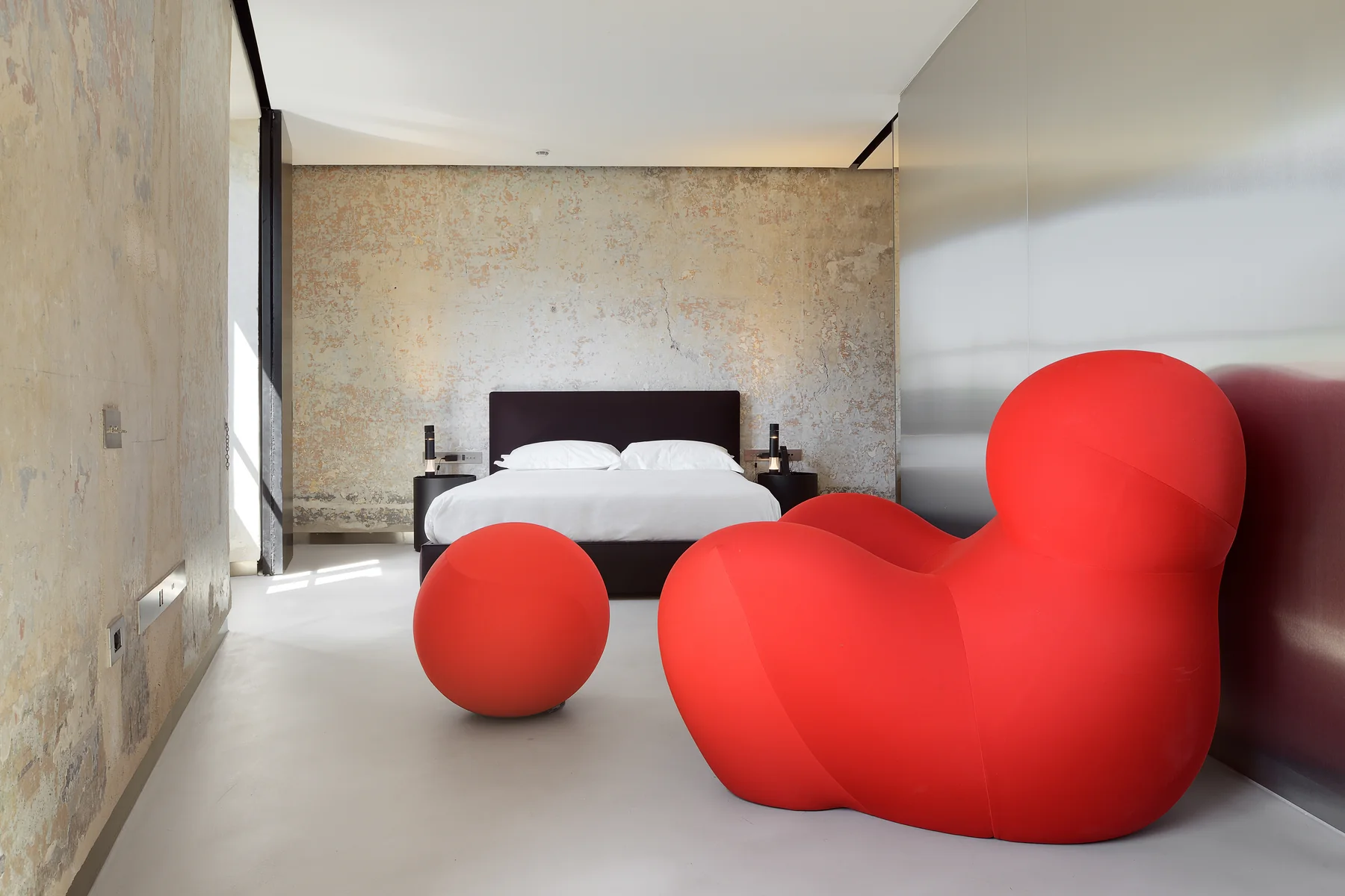 A suite at rhinoceros roma with a red sculptural sofa against raw plaster