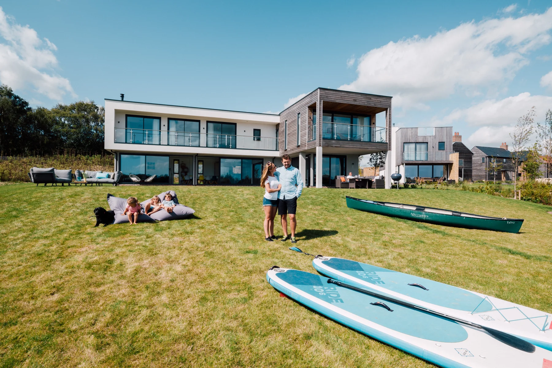 A family and paddleboards on the lawn of a contemporary holiday home at Silverlake, Dorset