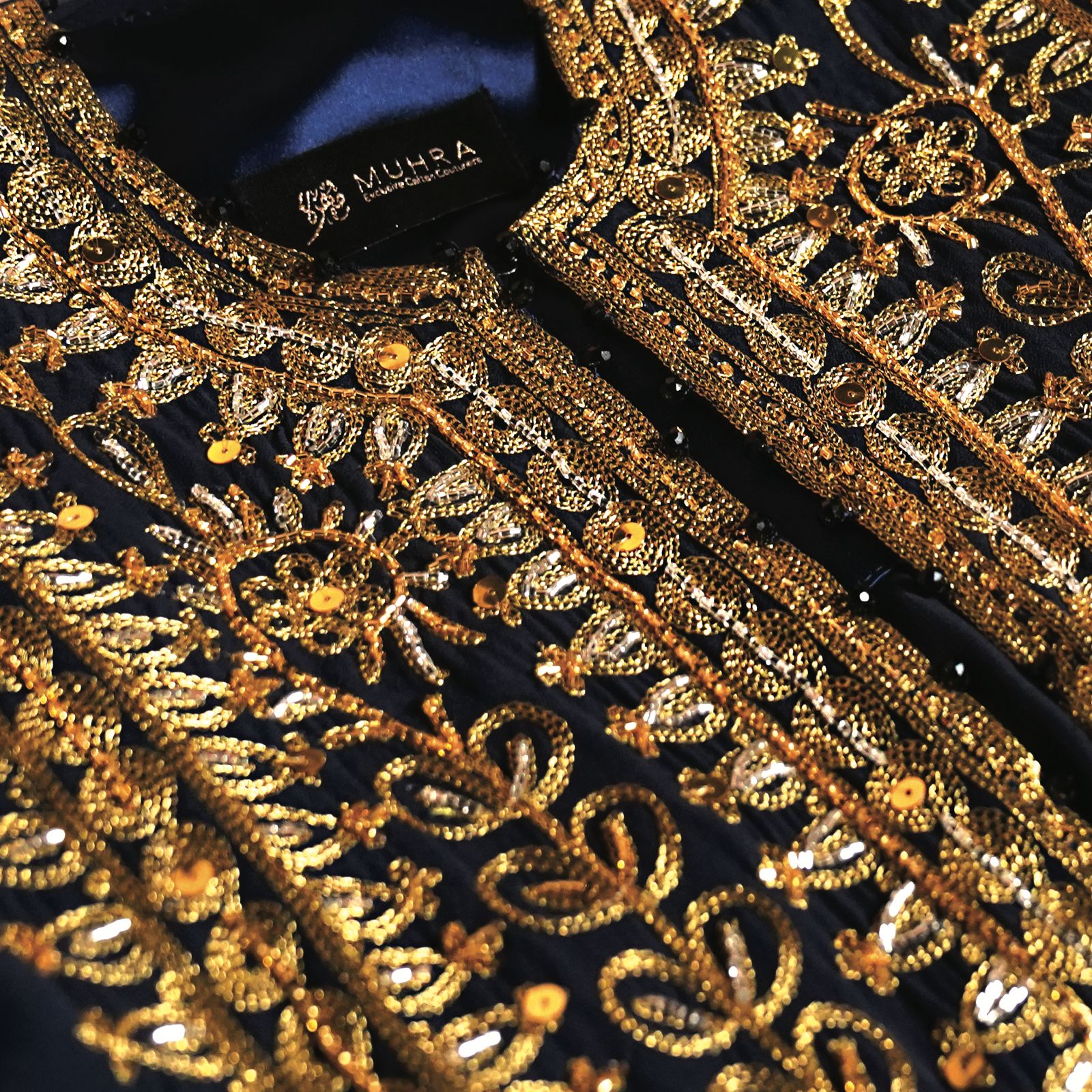 Close detail of gold thread embroidery on a dark Muhra thoub