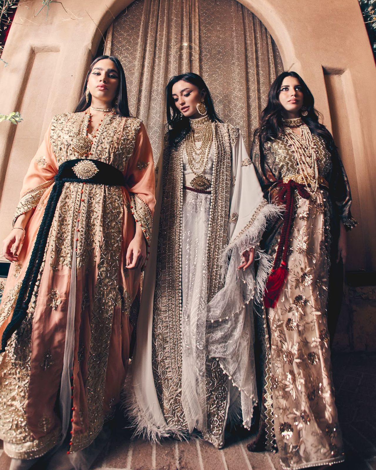 A blush-rose and an ivory Muhra thoub worn side by side, each with dense metallic embroidery
