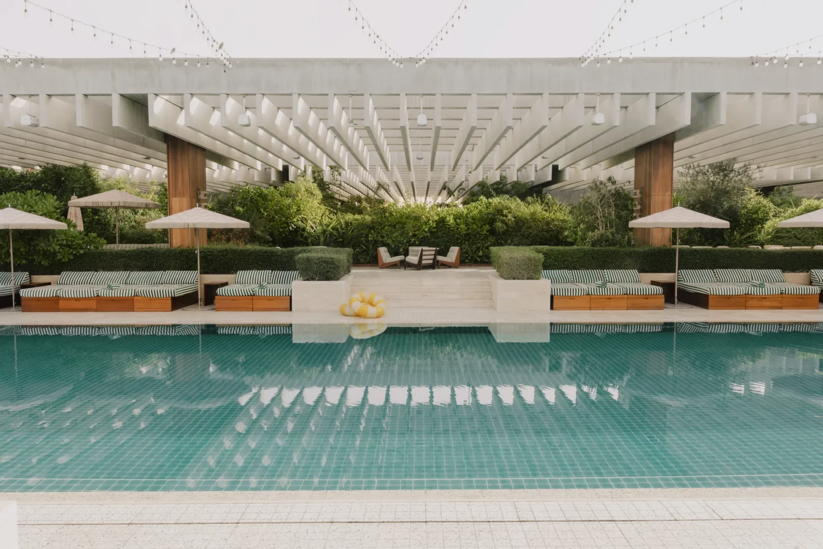 The garden pool at The Ned Doha framed by striped daybeds and greenery