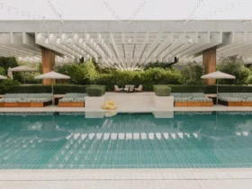 The garden pool at The Ned Doha framed by striped daybeds and greenery
