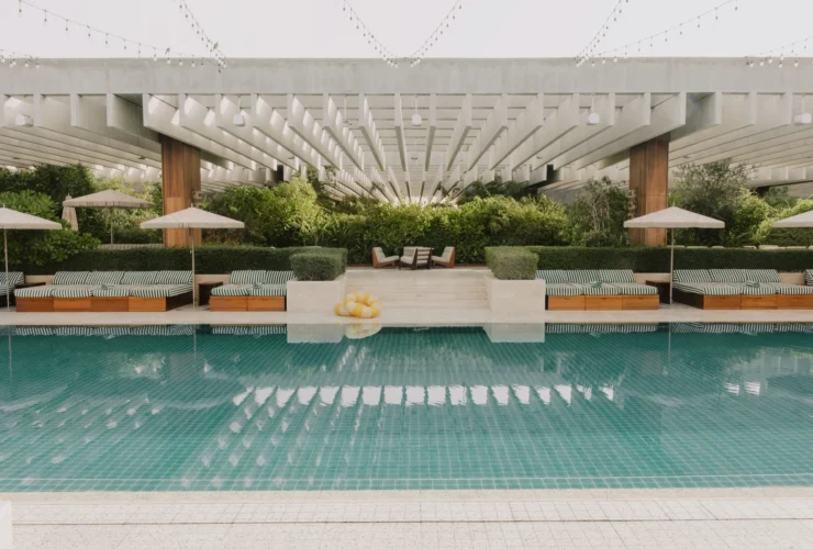 The garden pool at The Ned Doha framed by striped daybeds and greenery