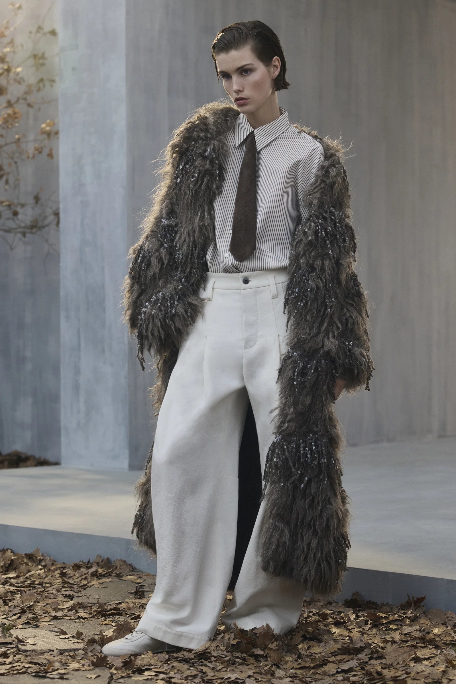 A model in a Brunello Cucinelli shearling coat and white wide-leg trousers, Fall Winter 2026