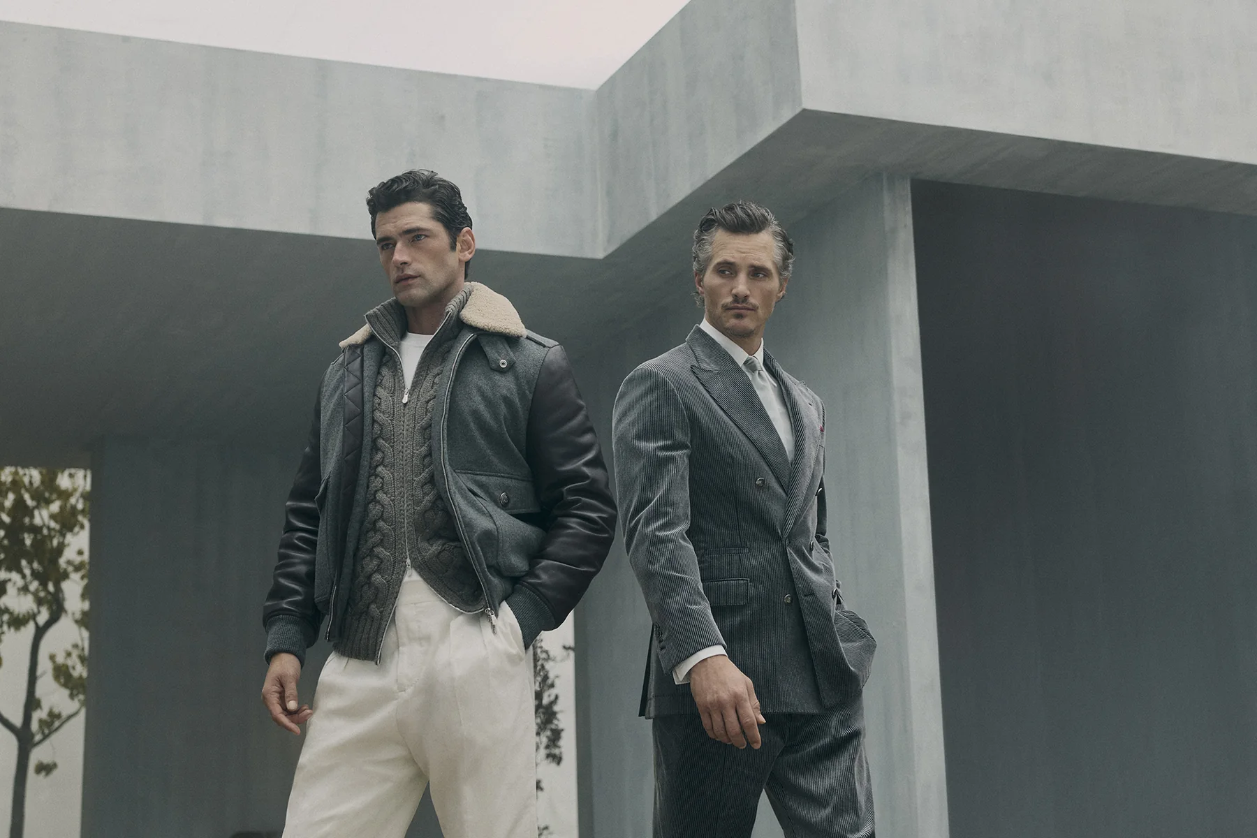 Two models in Brunello Cucinelli Fall Winter 2026, a shearling bomber and a grey double-breasted suit