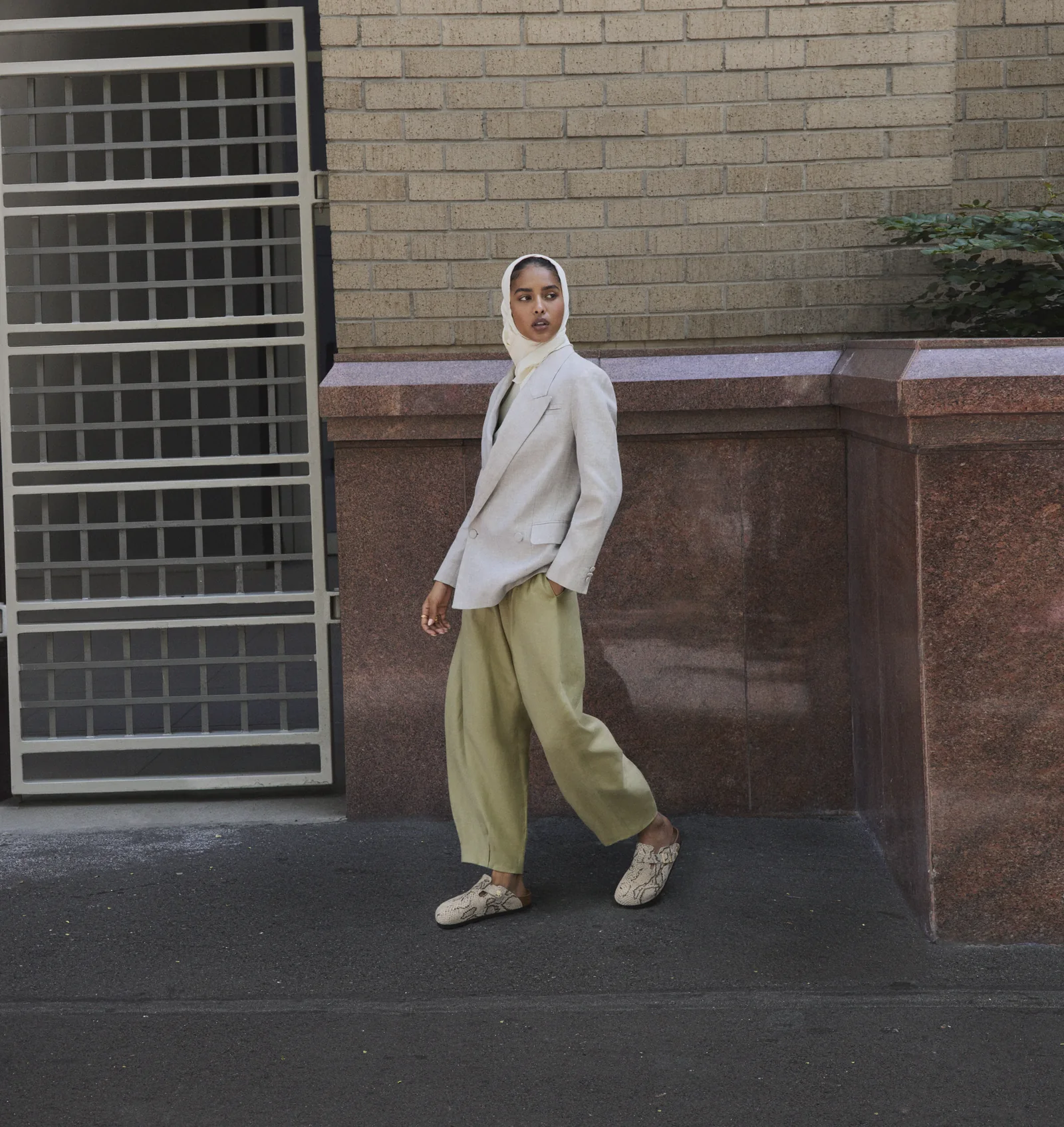 A model in a hijab, blazer and wide trousers wearing Birkenstock Animal Pack clogs on a city street