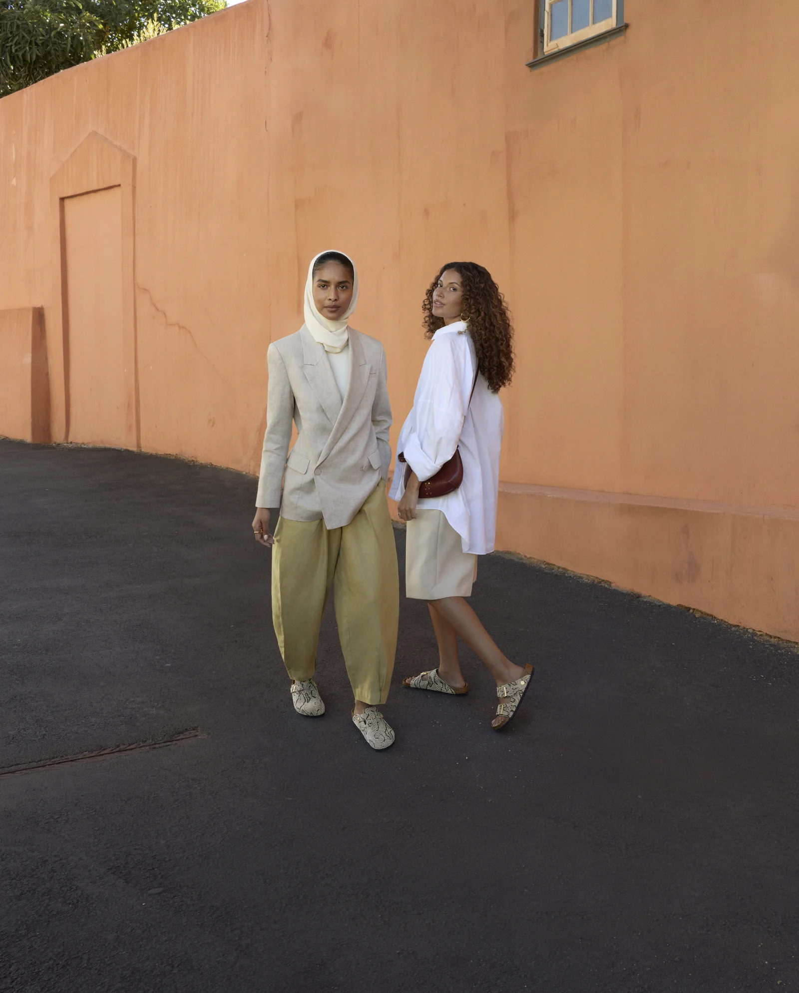 Two models in modest tailoring wearing Birkenstock Animal Pack sandals against a terracotta wall