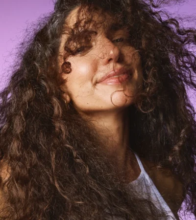 Model with curls smiling on a lilac backdrop, Sephora haircare campaign