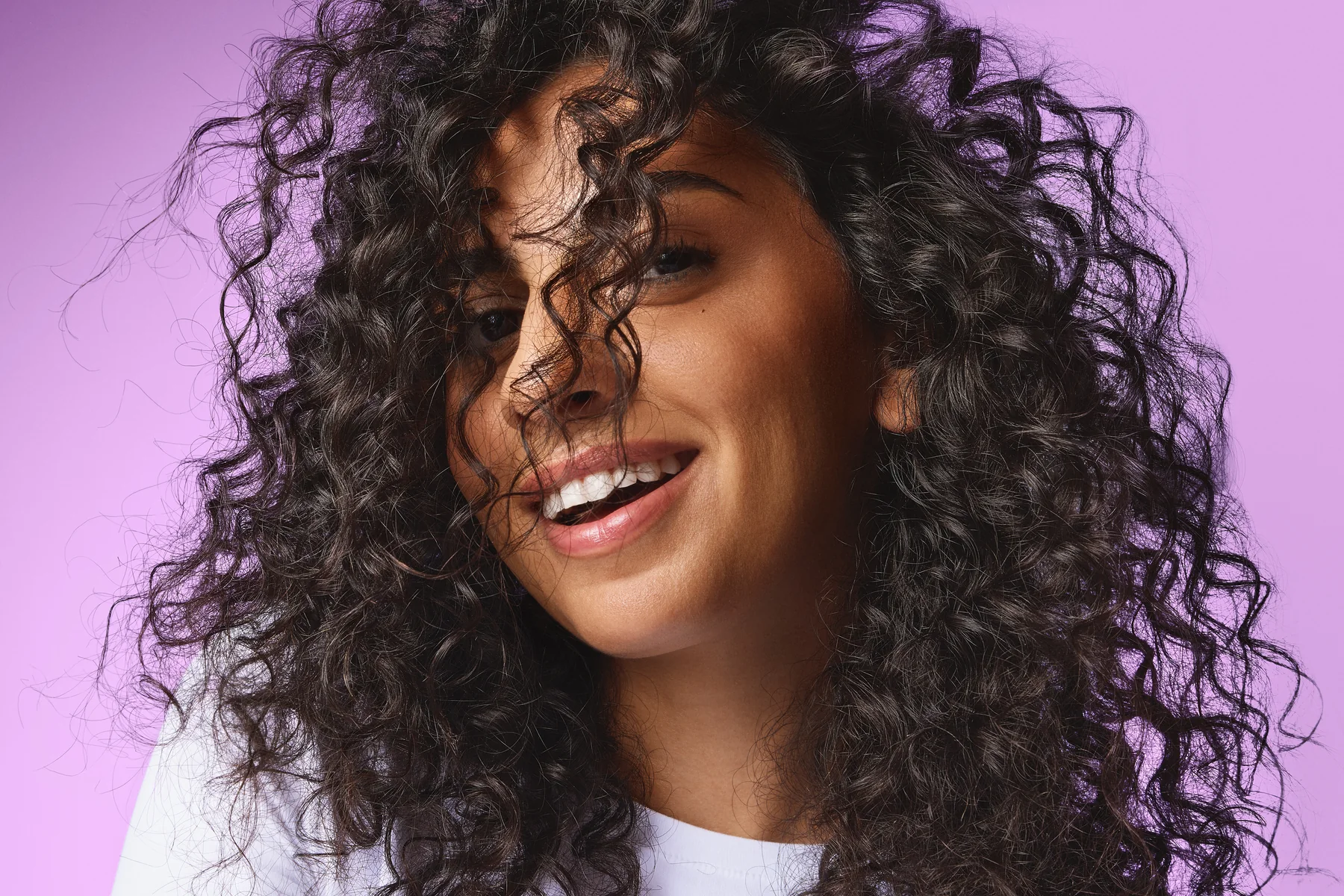 Model tending to curls on a lilac backdrop, Sephora haircare campaign