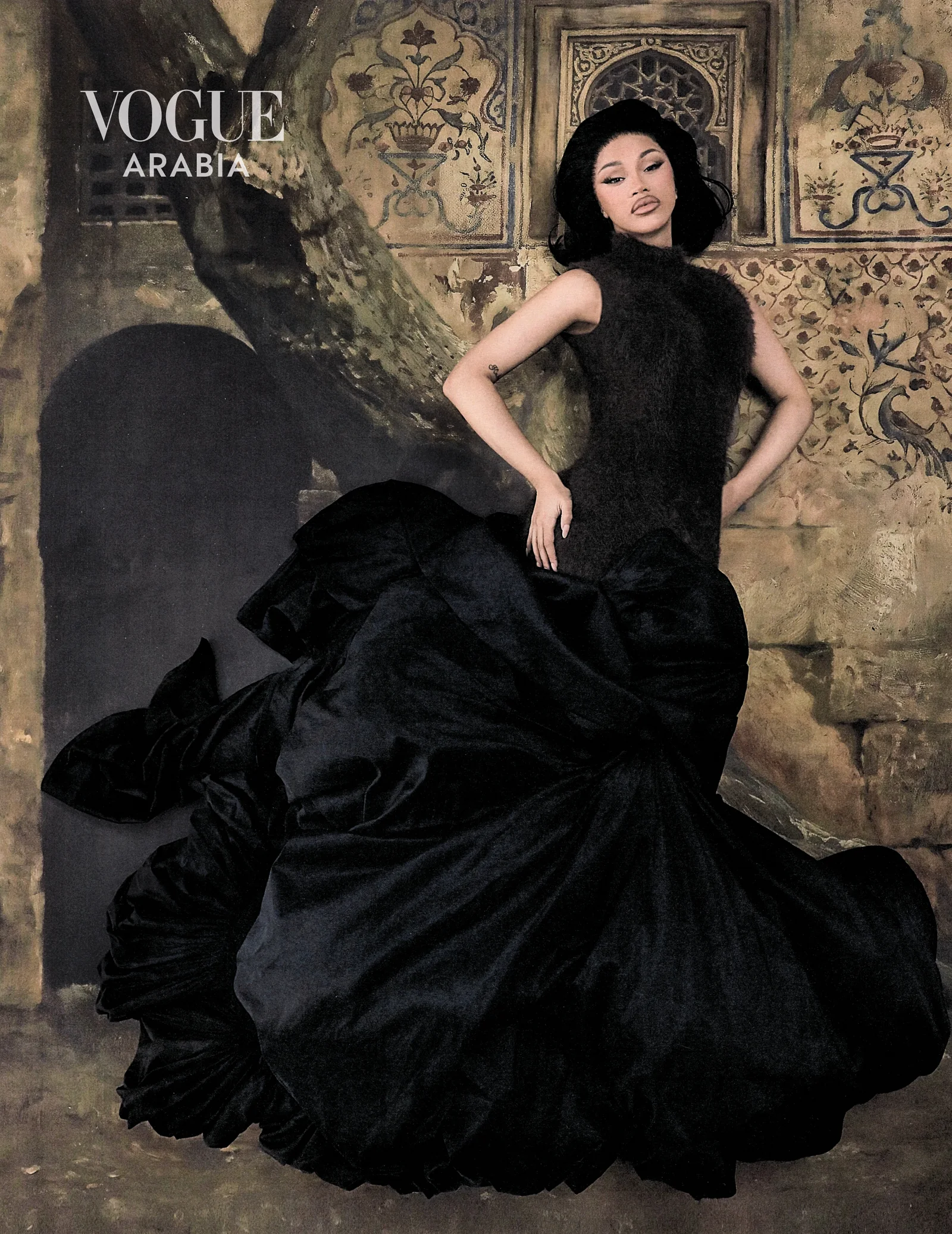 Cardi B in black taffeta against a carved stone arch for Vogue Arabia