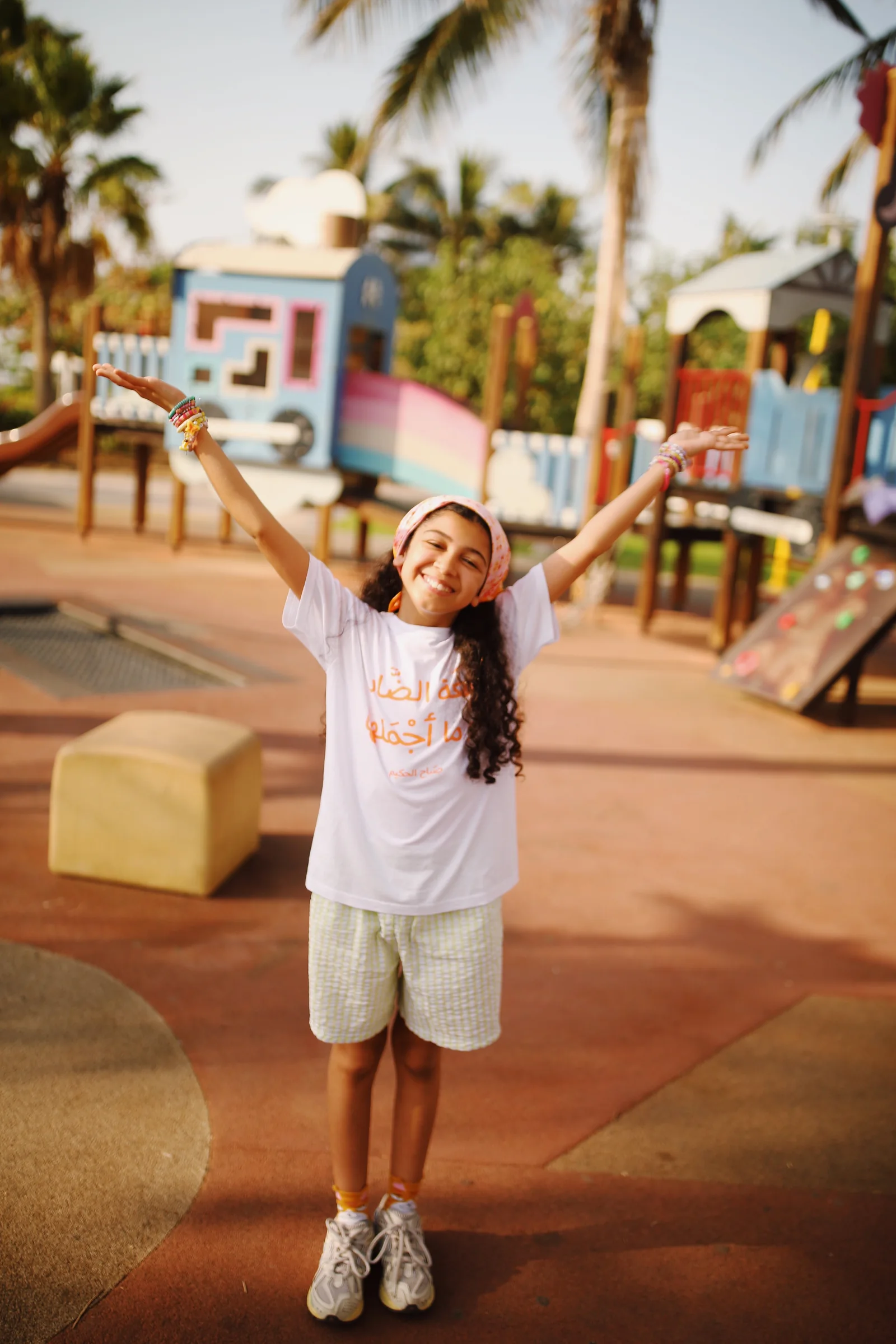 A child at a playground, arms raised in joy