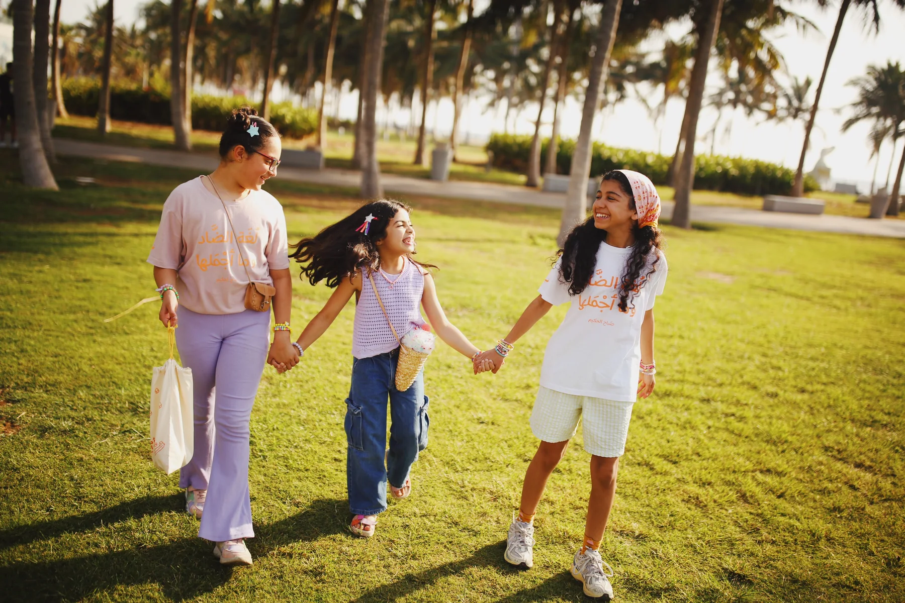 Three children walking hand in hand through a park at golden hour