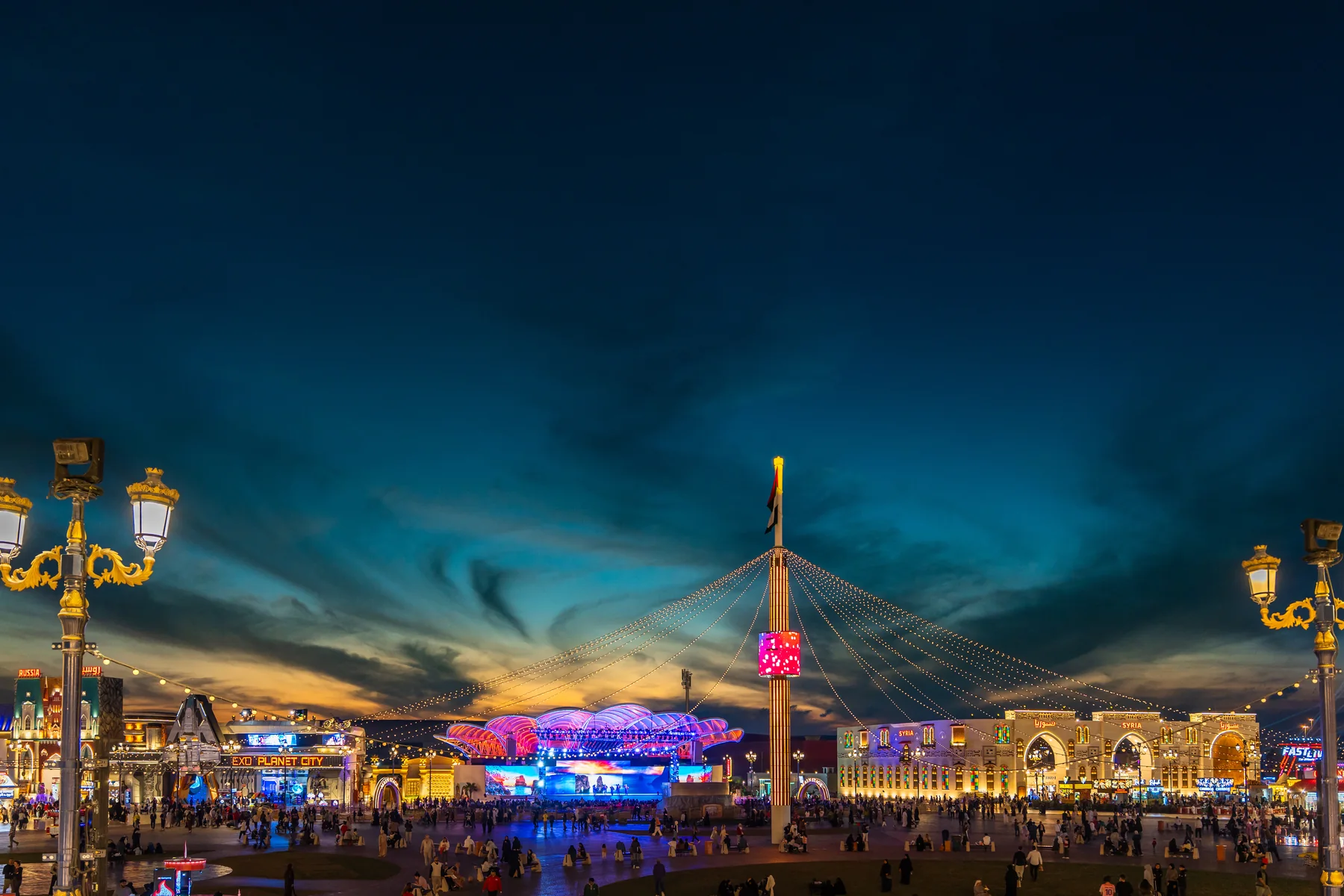 Global Village Dubai at dusk, illuminated bridge and pavilions